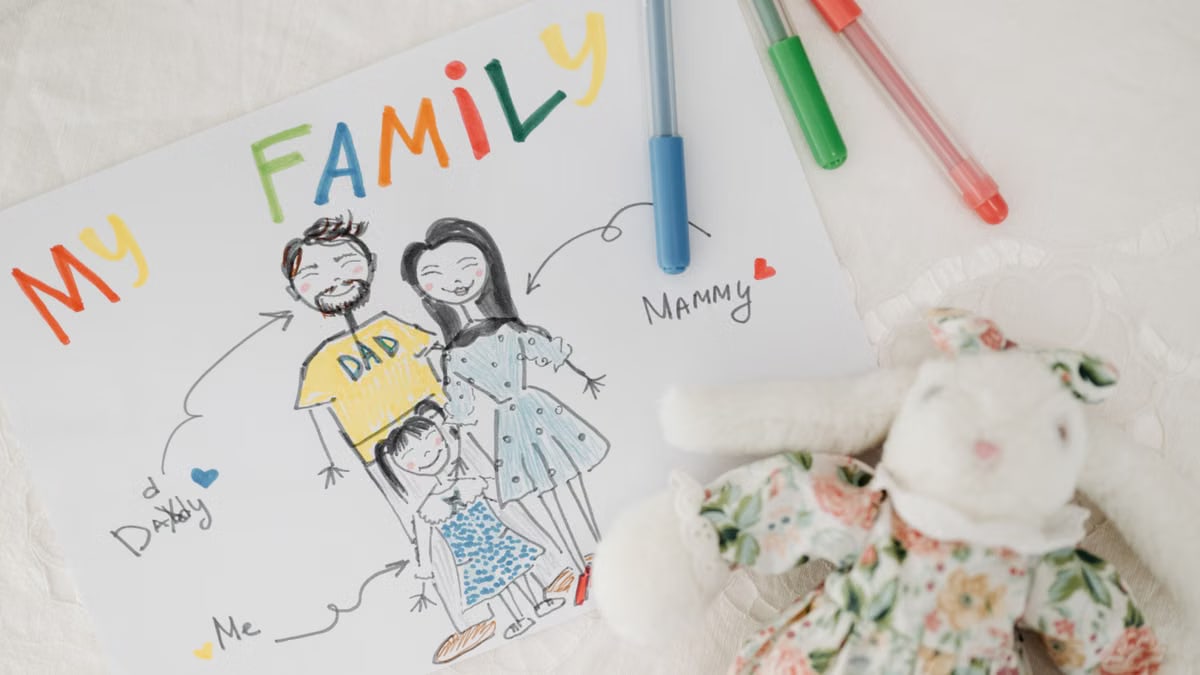A child's colorful family drawing next to pens and a plush toy on a white surface.